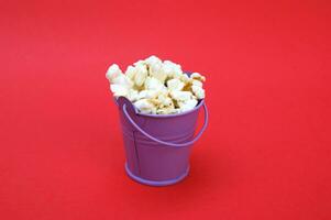 The fresh popcorn in a small decorative iron bucket on a red background. photo