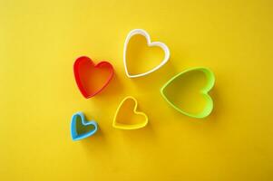 Plastic molds of multi colors for making cookies in the shape of a hearts on a yellow background. photo