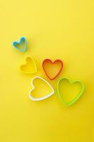 Plastic molds of multi colors for making cookies in the shape of a hearts on a yellow background. photo