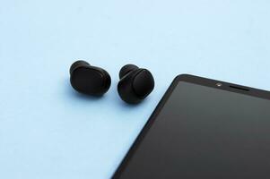 Smartphone and wireless headphones or earbuds with charging case on bright blue background. photo
