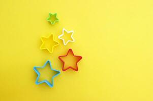 el plastico moldes de multi colores para haciendo galletas en el forma de un estrella en un amarillo antecedentes. foto