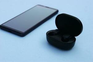 Smartphone and wireless headphones or earbuds with charging case on bright blue background. photo