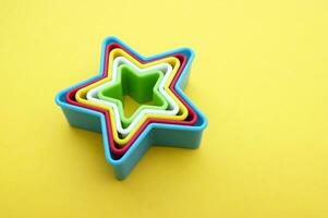 el plastico moldes de multi colores para haciendo galletas en el forma de un estrella en un amarillo antecedentes. foto