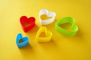 Plastic molds of multi colors for making cookies in the shape of a hearts on a yellow background. photo