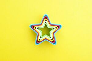 el plastico moldes de multi colores para haciendo galletas en el forma de un estrella en un amarillo antecedentes. foto