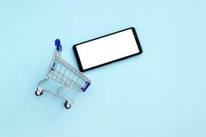 Shopping cart with a smartphone on a blue background. photo