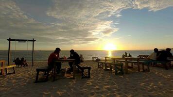 espaço de tempo do pessoas desfrutando pôr do sol às de praia restaurante. de praia cafeteria ou restaurante às dourado hora video