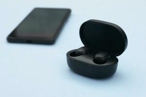 Smartphone and wireless headphones or earbuds with charging case on bright blue background. photo