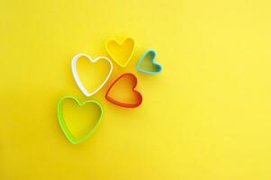 Plastic molds of multi colors for making cookies in the shape of a hearts on a yellow background. photo