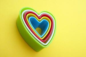 Plastic molds of multi colors for making cookies in the shape of a hearts on a yellow background. photo
