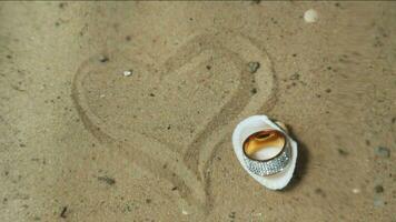 Precious ring in shell on sandy bottom, next to heart drawn in sand. video