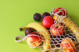 Red apples, bananas, plums and string bag on a bright green background. photo