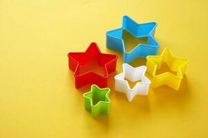 Plastic molds of multi colors for making cookies in the shape of a star on a yellow background. photo