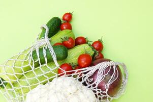 Ripe juicy red tomatoes, green cucumbers, zucchini and cauliflower in a string bag photo