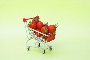 Organic cherry tomatoes in a mini shopping cart on a light green background. photo