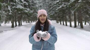 Young Beautiful Girl in a good mood blows snow from her hands while standing in the winter forest. slow motion video