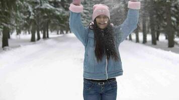 lindo menina dentro uma Boa humor lança neve sobre dela cabeça e fiação dentro a inverno floresta video