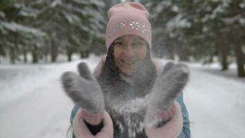 A beautiful girl shakes off snow from mittens and smiles while standing in a winter forest video