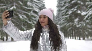 giovane bellissimo ragazza fabbricazione autoscatto utilizzando smartphone mentre in piedi nel il inverno foresta video