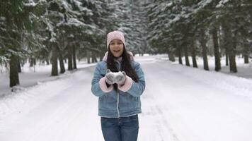 Young Beautiful Girl in a good mood blows snow from her hands while standing in the winter forest and smiling. slow motion HD video