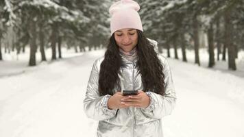 un atractivo joven niña camina mediante el invierno bosque y usos un teléfono inteligente 4k video