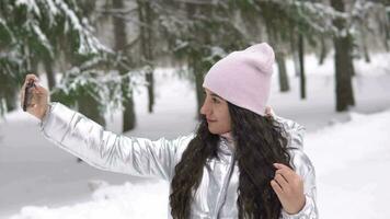 Beautiful girl makes selfie using a smartphone in the winter forest 4K video