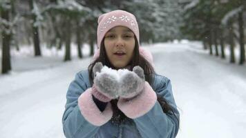 lindo menina dentro uma Boa humor golpes neve a partir de a mãos dentro a inverno floresta video