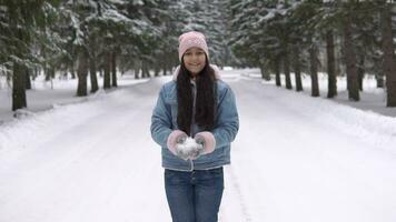 jovem lindo menina dentro uma Boa humor golpes neve a partir de dela mãos enquanto em pé dentro a inverno floresta e sorridente. lento movimento video