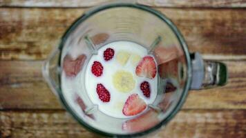 fresco fragole, banane e latte siamo misto nel un' miscelatore su il tavolo. Visualizza a partire dal sopra. video