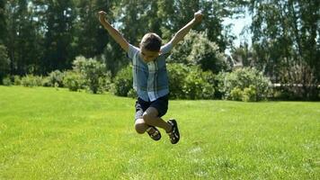 An attractive little boy runs along the grass in the park having a good mood in sunny weather. slow motion. video