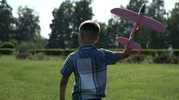 The Little Boy runs a toy plane in the park in sunny weather. slow motion. video