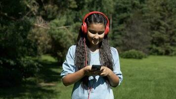 un atractivo joven niña con largo pelo paseos mediante el parque y escucha a música en auriculares.lento movimiento. video