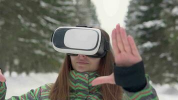 een jong mooi vrouw toepassingen elektronisch virtueel realiteit bril buiten in een besneeuwd Woud in winter. langzaam beweging video