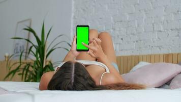 verde pantalla, modelo para publicidad, cromo llave, universal pantalla táctil. un mujer carreras en un pantalla táctil con su dedo desde el fondo arriba mientras acostado en el cama video