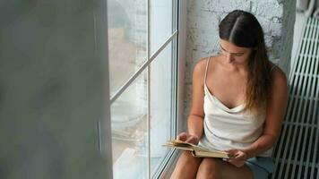 Leisure at home, Stay in the house, Beautiful woman, home weekend. Woman reading a book while sitting on the floor near the window at home video