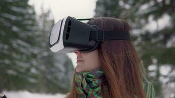 Young beautiful woman uses electronic virtual reality glasses outside in the forest in winter video