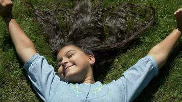 attraente giovane ragazza con nero capelli bugie su il erba nel il parco. lento movimento. HD video