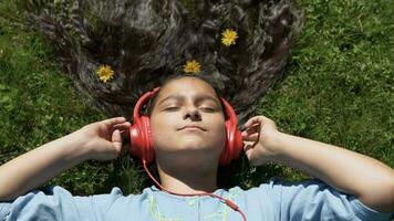 magnifique fille avec longue cheveux mensonges sur le herbe dans le parc et écoute à la musique dans casque.lent mouvement. HD video