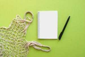 Reusable shopping bag and notebook with pen on green background. photo