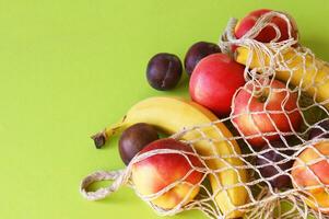 Red apples, bananas, plums and string bag on a bright green background. photo