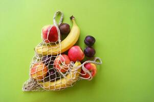 Red apples, bananas, plums and string bag on a bright green background. photo