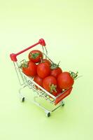 orgánico Cereza Tomates en un mini compras carro en un ligero verde antecedentes. foto