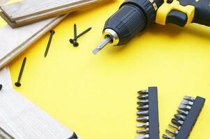 Yellow-black screwdriver on a yellow background, screws, a set of bits. photo