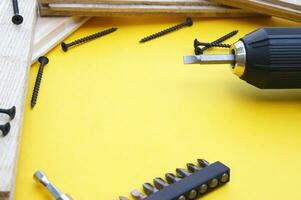 Yellow-black screwdriver on a yellow background, screws, a set of bits. photo