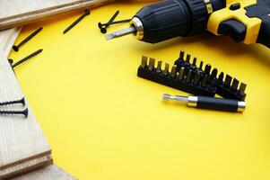 Yellow-black screwdriver on a yellow background, screws, a set of bits. photo