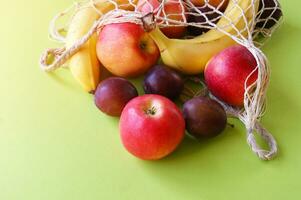 Red apples, bananas, plums and string bag on a bright green background. photo