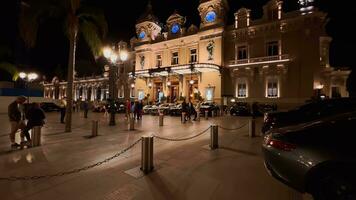 Monaco, monte Carlo, 21 Oktober 2022 - - Platz Kasino Monte Carlo beim Dämmerung, ein Menge von Luxus Autos, Hotel de Paris, Reichtum Leben, Touristen nehmen Bilder von das Wahrzeichen, Kiefer Bäume, Blau Himmel, Blumen video