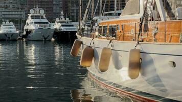 Sun glare on the wooden side of a sailing boat in classic style, a lot of huge mega yachts are moored in port Hercules by Monaco at sunset, residential complex Monte-Carlo on background video