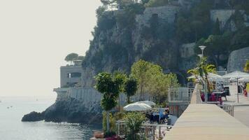 Mônaco, monte carlo, 25 Outubro 2022 - cafeteria aterro em a cais dentro a porta do Mônaco, uma montanha dentro a fundo às ensolarado dia, pessoas estão sentado dentro cafeteria, uma Lugar, colocar para banhos de sol video