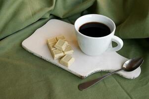 White cup with fresh coffee with a white bar of chocolate with whole hazelnuts. photo